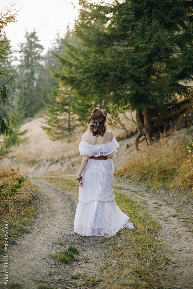 girl behind in a white dress on th road between the woods in the mountains