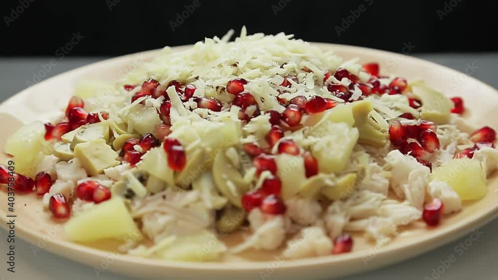 A woman's hand pours parmesan cheese into a plate with a salad of chopped chicken fillet and mushrooms and pineapples. Medium plan A woman's hand pours parmesan cheese into a plate with a salad of chopped chicken fillet and mushrooms and pineapples. Medium plan