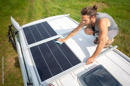 Fotografie, Obraz Man cleaning a solar panel on the roof of a camper van