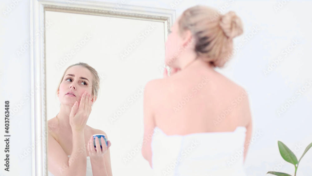 Pretty female applying cream on face while looking at mirror reflection in cozy bathroom. Pretty female applying cream on face while looking at mirror reflection in cozy bathroom.
