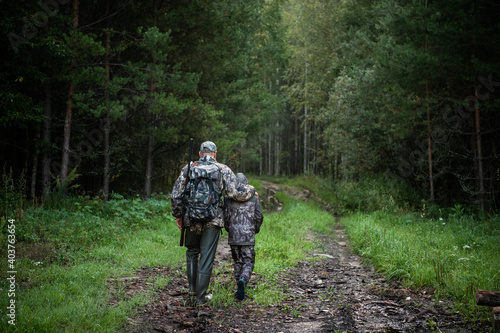 Hunters with hunting equipment going away through rural forest at sunrise during hunting season in countryside.