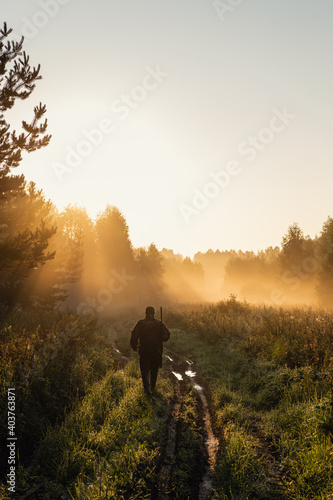 Hunter with a shotgun in his hands walking on a foggy morning on a rural road in a forest