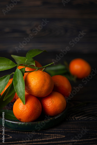 Sweet juicy orange New Year's clementine tangerines, mandarines with green leaves. Citrus still life on a brown wooden background. Healthy winter fruits with vitamin C to boost immunity. Copy space