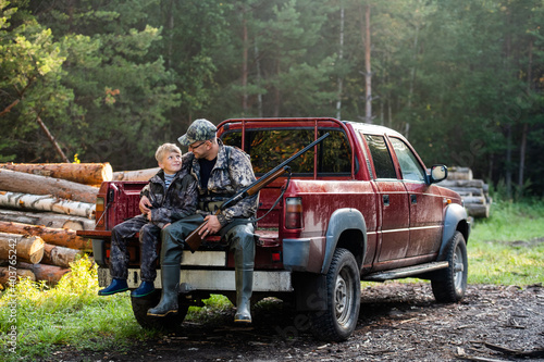 Tableau sur toile Father and son sitting together in truck outdoors with shotgun hunting gear