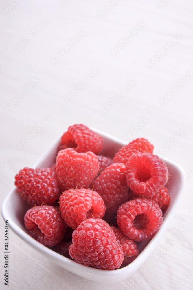 Bowl of fresh raspberries with green leaves on wooden background. Top view Bowl of fresh raspberries with green leaves on wooden background. Top view
