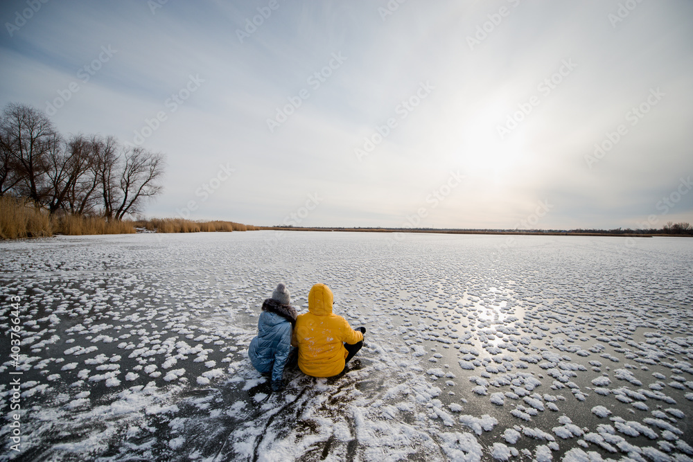 a couple in love sits on the ice of a frozen lake and admires the beautiful sunset