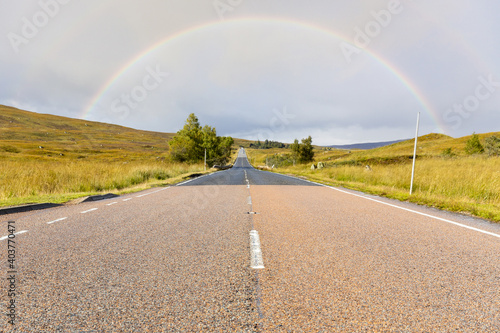 Empty road in the highlands, Scotland, leading to a rainbow - Travel and transportation concept with Scottish landscape on background near Glencoe