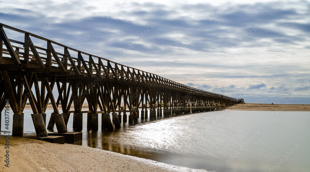 long wooden boardwalk pier leads from one beach to another over a small ocean inlet