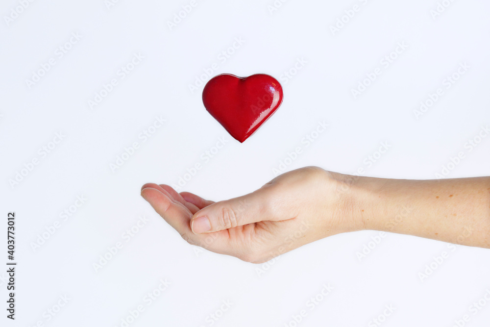 Red love heart levitating upon an outstretched female hand against white background. Love concept.