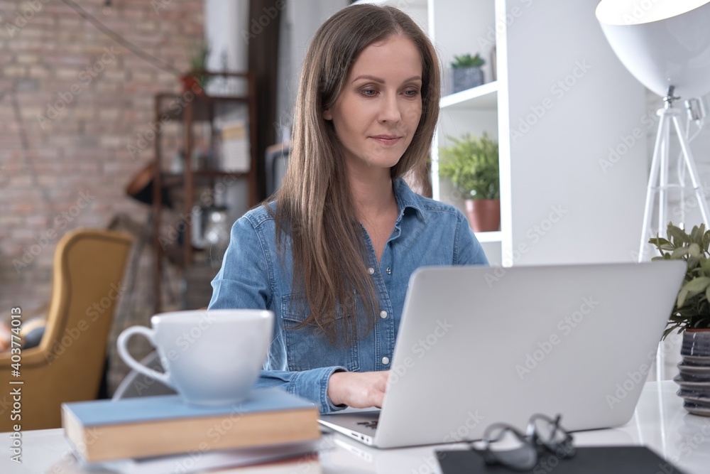 Happy white young business woman working at home with laptop computer, coffee, books on desk. Happy white young business woman working at home with laptop computer, coffee, books on desk.