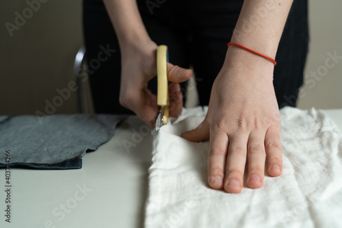 Women's hands cut fabric on a paper pattern with tailor's scissors on a white table. A dressmaker at work in a sewing studio.