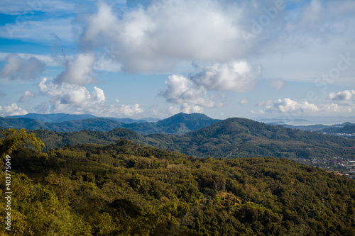 The landscape of the mountain ridge of Phuket and the Adaman Sea against the background of a blue sky with clouds.