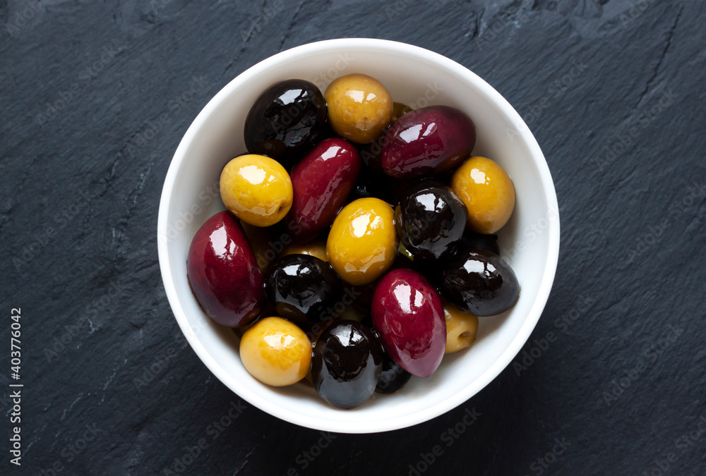 Different kinds of organic ripe olives on oil in the white bowl on the dark stone background macro close up Different kinds of organic ripe olives on oil in the white bowl on the dark stone background macro close up