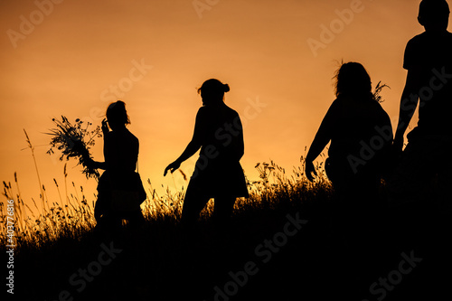 Silhouettes of People picking flowers during midsummer soltice celebraton against the background of sunset photo