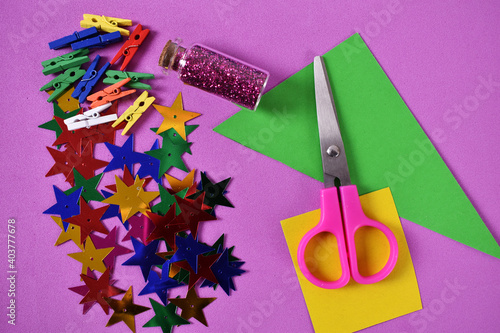 Pink scissors color stars with green and yellow paper on violet background