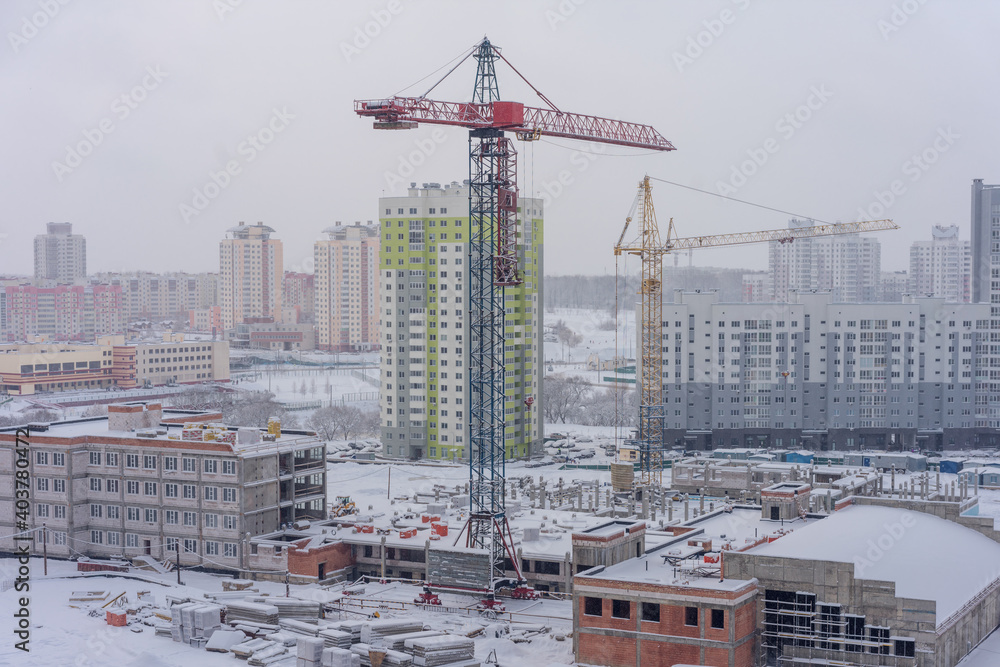 Construction site with crane and unfinished buildings covered with white snow