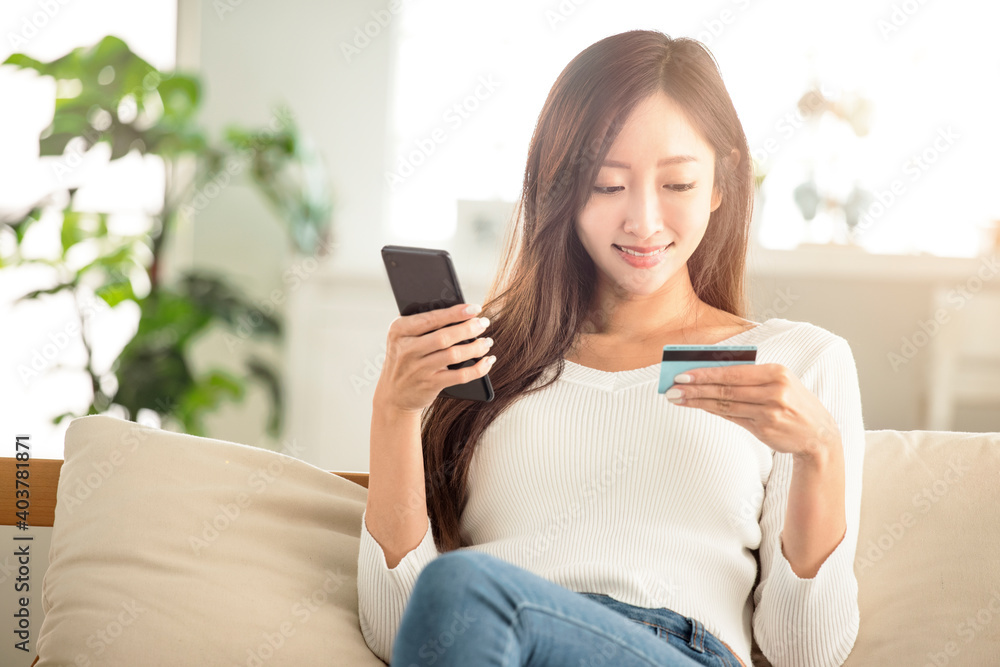young woman buying online with credit card and smart phone sitting on couch at home young woman buying online with credit card and smart phone sitting on couch at home