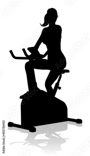 A woman in silhouette using a stationary exercise spin bike piece of gym equipment fitness machine