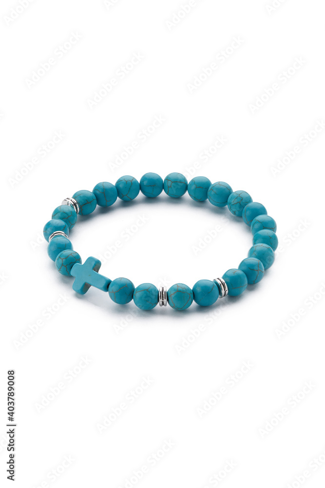 Detailed shot of blue bracelet made of turquoise beads with veins and decorated with silver charms and blue stone cross. The stylish bracelet is isolated on the white background. Detailed shot of blue bracelet made of turquoise beads with veins and decorated with silver charms and blue stone cross. The stylish bracelet is isolated on the white background.