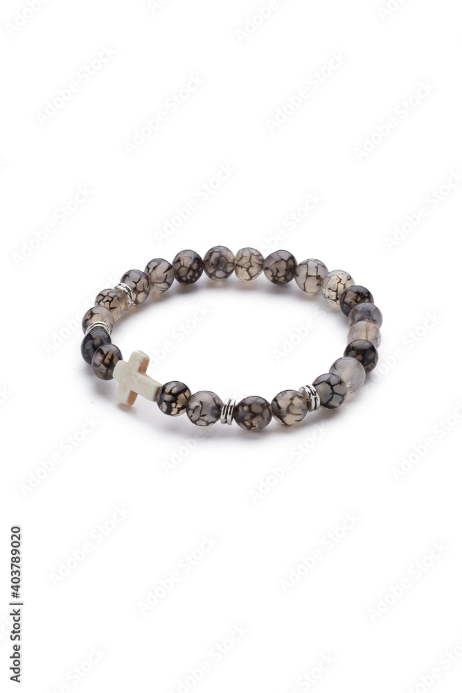 Detailed shot of gray bracelet made of translucent beads with veins and decorated with silver charms and ivory stone cross. The stylish bracelet is isolated on the white background. Detailed shot of gray bracelet made of translucent beads with veins and decorated with silver charms and ivory stone cross. The stylish bracelet is isolated on the white background.