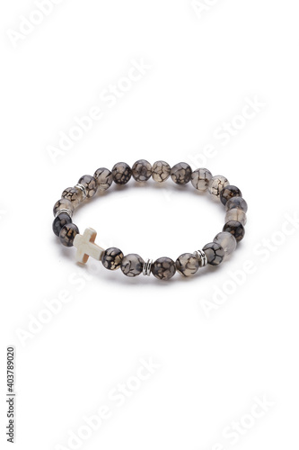 Detailed shot of gray bracelet made of translucent beads with veins and decorated with silver charms and ivory stone cross. The stylish bracelet is isolated on the white background. 