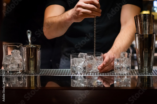Male bartender's hands chilling out cocktail glasses. Bartender's hands mixing ice with bar spoon to chill cocktail glassware.