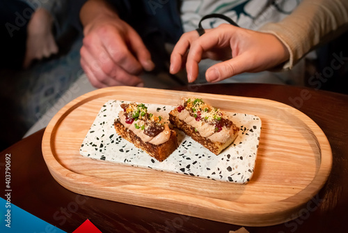 party snacks. two mini toasts with pate served on wooden board. a couple tasting appetizers with pate. served snacks. one bite mini appetizers for party. canapes with pate served on wooden tray.
