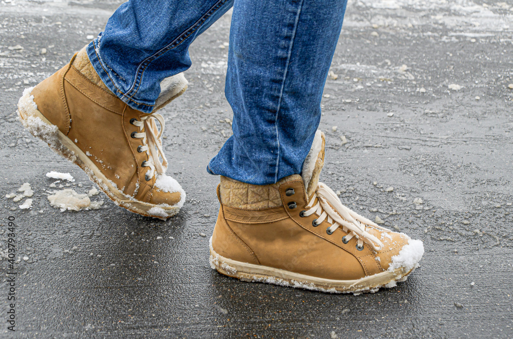 Women's foots in jeans and demi-season suede boots on asphalt with snow and reagents. Use of reagents when cleaning city streets from snow, damage to suede and leather shoes. Women's foots in jeans and demi-season suede boots on asphalt with snow and reagents. Use of reagents when cleaning city streets from snow, damage to suede and leather shoes.