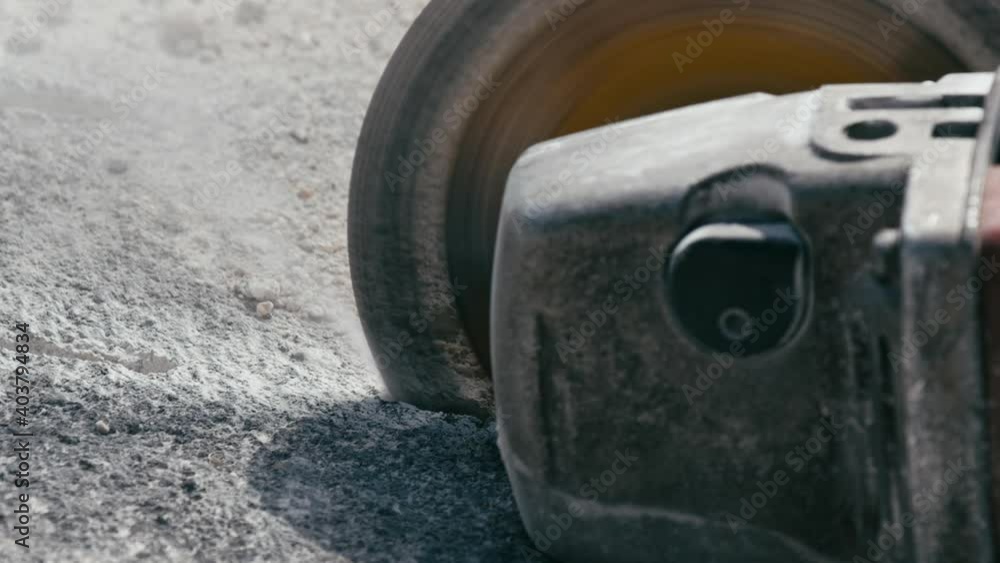 Cutting the concrete slab with electric circular saw. Construction worker cutting concrete floor and dust fly around, slow motion, close up
