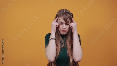 Headache grimacing pain holds the back of neck indicating location. Fatigue during workaholism labor. Young attractive woman, dressed green shirt blonde hair, yellow background