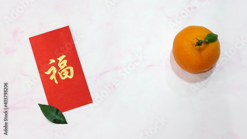 A mandarin orange with red ang pow (a monetary gift given during special occasions in Chinese culture, especially Chinese New Year). On the red angpow (red packet) is the chinese character 'fu'. photo