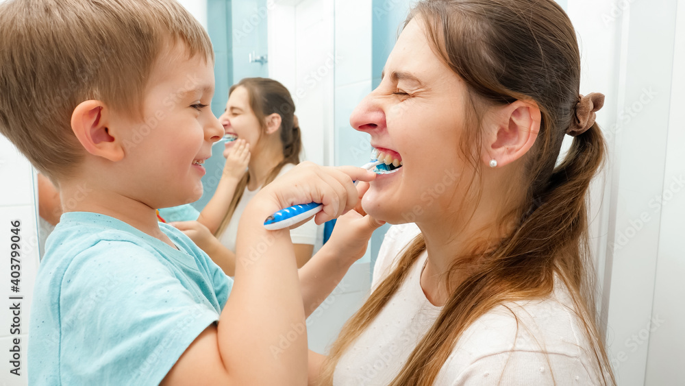 Funny toddler boy cleaning and brushing mothers teeth. Concept of family hygiene and teeth healthcare Funny toddler boy cleaning and brushing mothers teeth. Concept of family hygiene and teeth healthcare