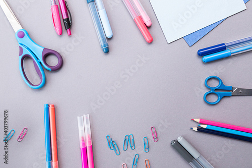 Various stationery in pink and blue colors, blank sheets of paper, on a gray background with copy space. Flat lay with pencils, scissors, pens, paper clips, felt-tip pens and sheets of paper.