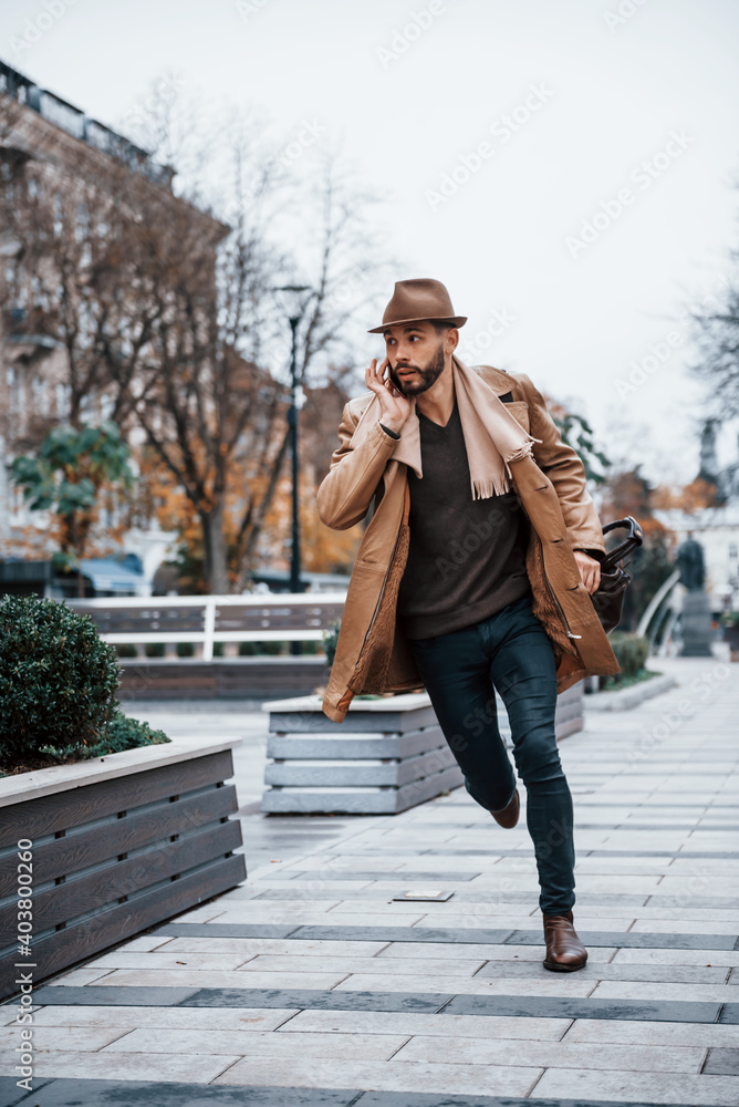 Running, late for meeting. Young male model in fashionable clothes is outdoors in the city at daytime Running, late for meeting. Young male model in fashionable clothes is outdoors in the city at daytime