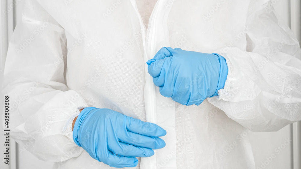 Fototapeta premium Closeup of female doctor of bacteriologist wearing and putting on protective biohazard suit, glasses, gloves and facial medical mask respirator against covid-19 and coronavirus
