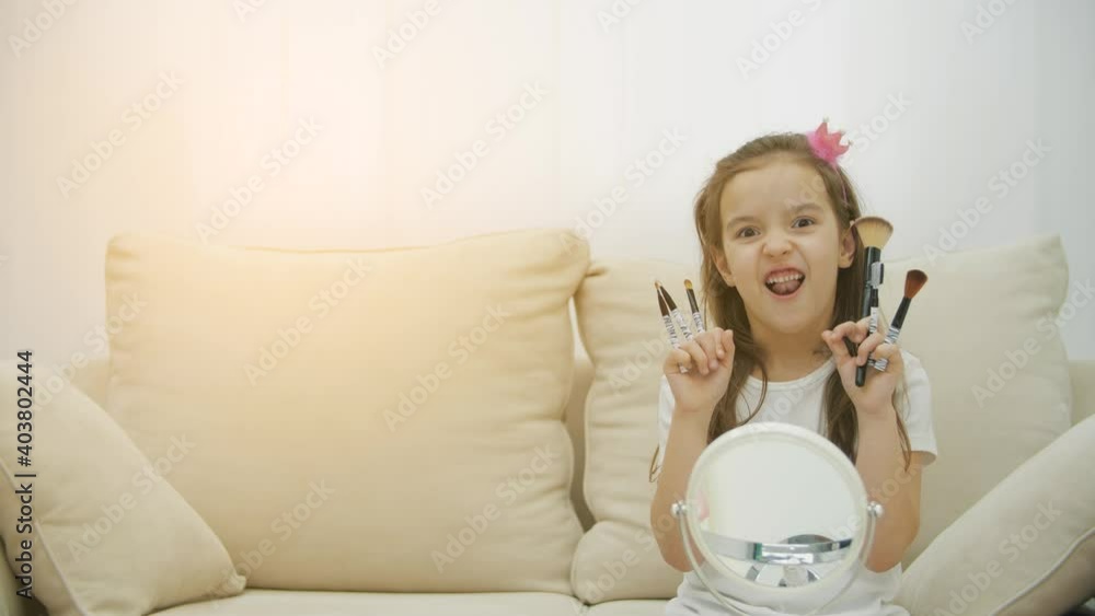 4k slowmotion video of smiling chils girl holding cosmetic brushes in the living room. 4k slowmotion video of smiling chils girl holding cosmetic brushes in the living room.