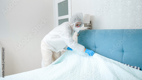 Hotel maid in protective medical suit and gloves tidying hotel room. Desinfection and hygiene during covid-19 and coronavirus pandemic photo