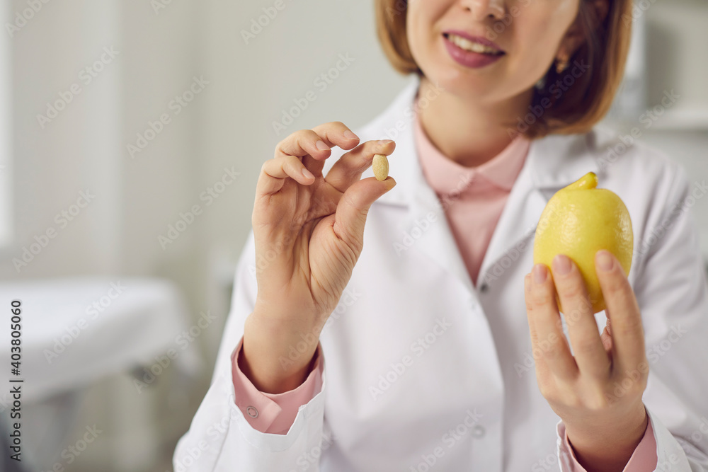 Doctor holding fresh lemon and yellow vitamin C or dietary food supplement pill. Concept of health care, treatment, flu and cold prevention, choice between natural and synthetic medicine. Close-up Doctor holding fresh lemon and yellow vitamin C or dietary food supplement pill. Concept of health care, treatment, flu and cold prevention, choice between natural and synthetic medicine. Close-up