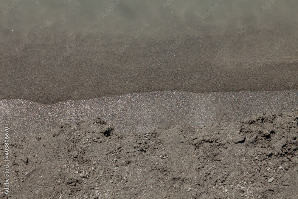 Obraz premium Close-up of a sandy shore with gray sand on the beach of a mountain river with a running washing wave on the coastline. Background for wallpaper, post or illustrations in social networks.