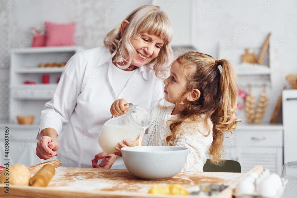 Fills with milk. Senior grandmother with her little granddaughter cooks sweets for Christmas on the kitchen Fills with milk. Senior grandmother with her little granddaughter cooks sweets for Christmas on the kitchen