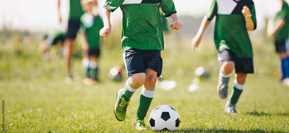 Kids running after soccer ball at natural grass sports field. Group of children training football skills at physical education class. Sports summer practice for kids with coach Kids running after soccer ball at natural grass sports field. Group of children training football skills at physical education class. Sports summer practice for kids with coach