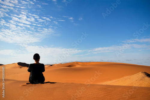 A woman is sitting on the golden sand dune of the Namib desert. Africa