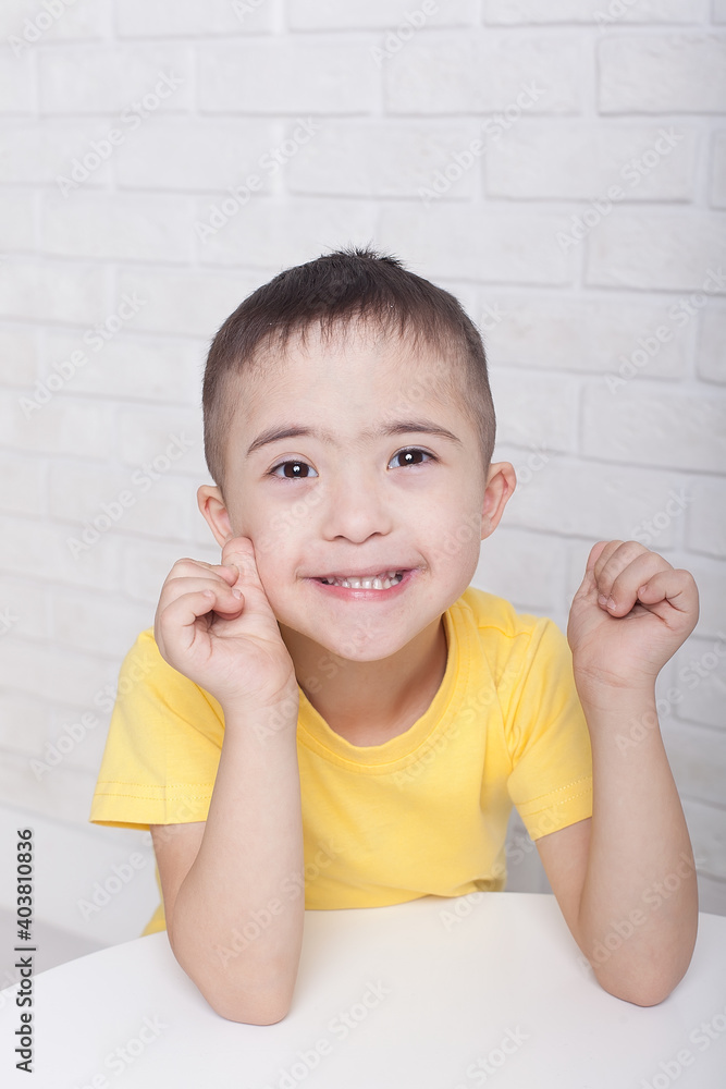 Cute boy with Down syndrome in glasses sitting, smiling at the camera and playing Cute boy with Down syndrome in glasses sitting, smiling at the camera and playing