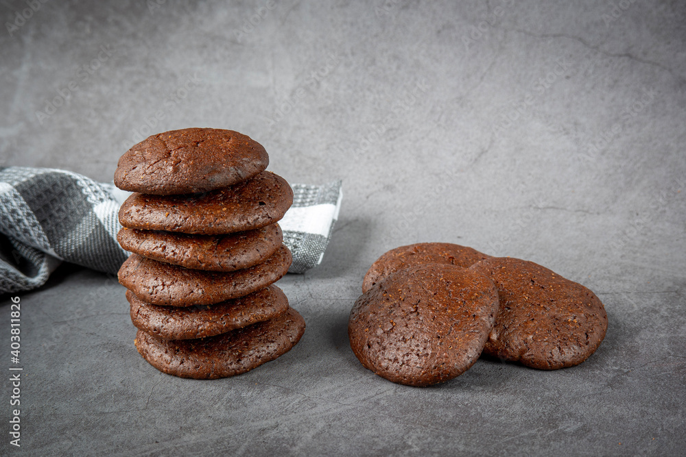 Stack of fluffy chocolate brownie cookies along with pieces of dark chocolate and a towel on a gray background. Healthy homemade gluten free chocolate chip cookies. 