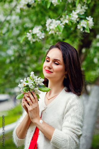 Brunette in flowers. The girl hugs a large bouquet of white flowers and smiles with her eyes closed. A young woman in flowers with her eyes closed. One-stop blooming in the spring