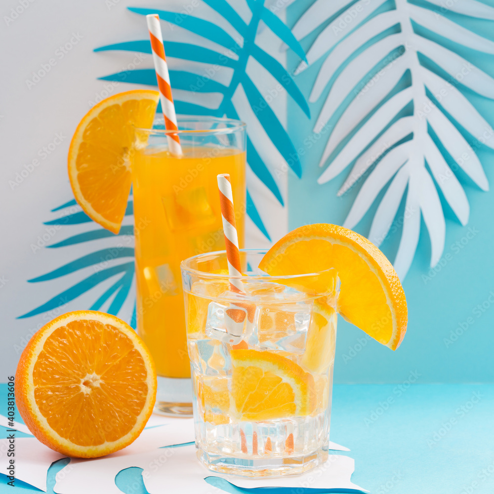 Cold orange juice drink in glass, fresh citrus and palm leaves on blue and white background. Cold orange juice drink in glass, fresh citrus and palm leaves on blue and white background.