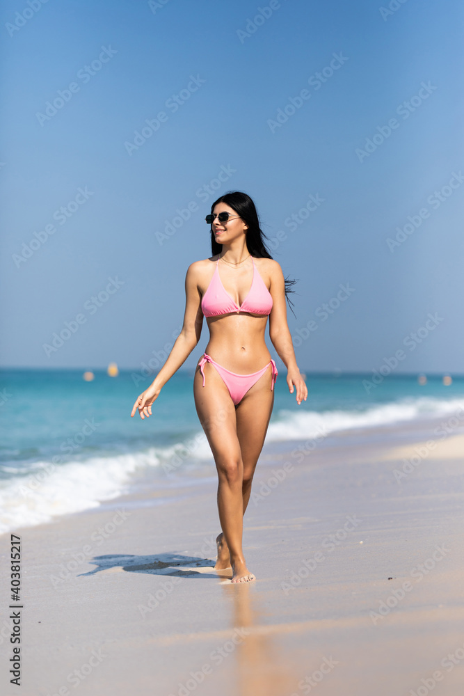 Young sexy woman in bikini walking away on the idyllic beach