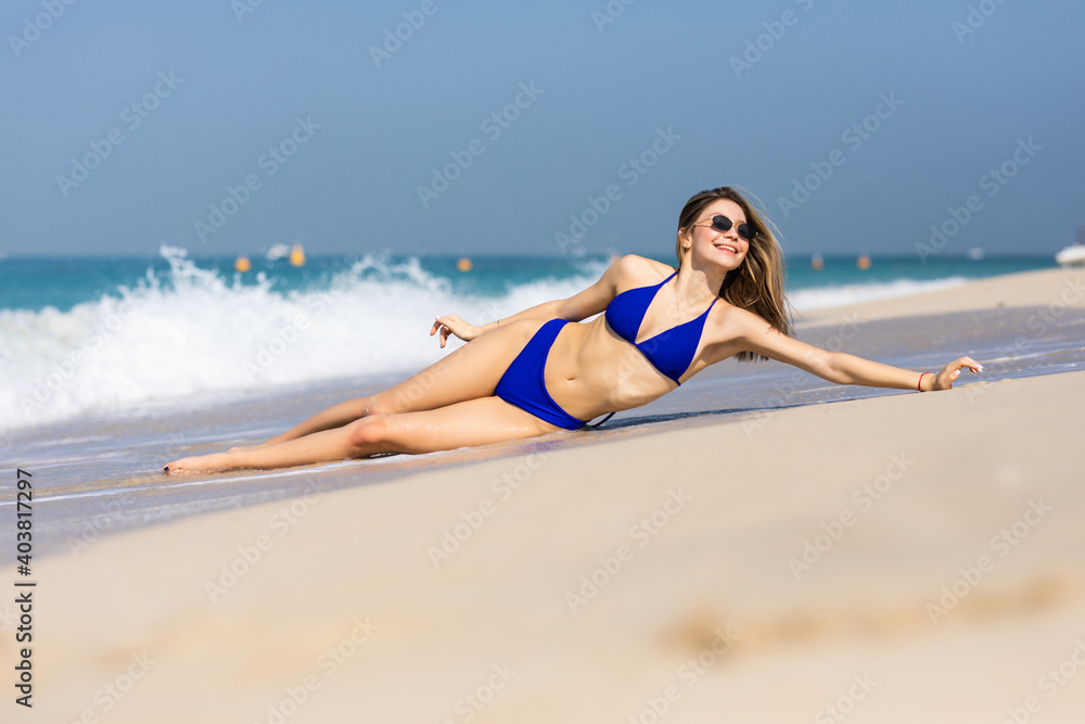 Young beautiful woman lying on the wet sand against ocean and blue sky