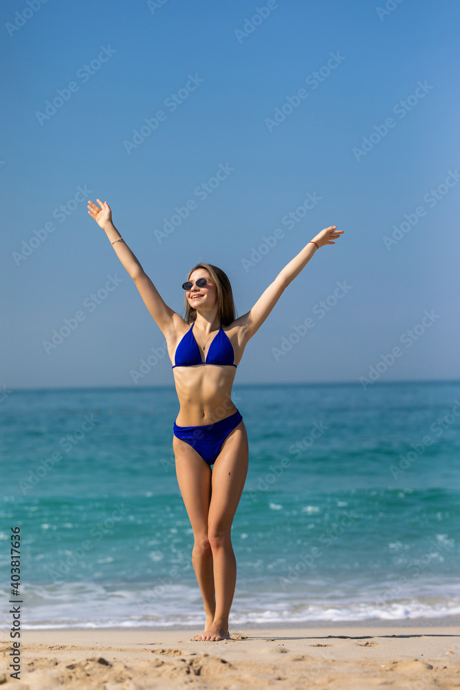 Beautiful young woman with raised hands, looking at ocean. Freedom concept, holiday, beach, clear sky background. Beautiful young woman with raised hands, looking at ocean. Freedom concept, holiday, beach, clear sky background.