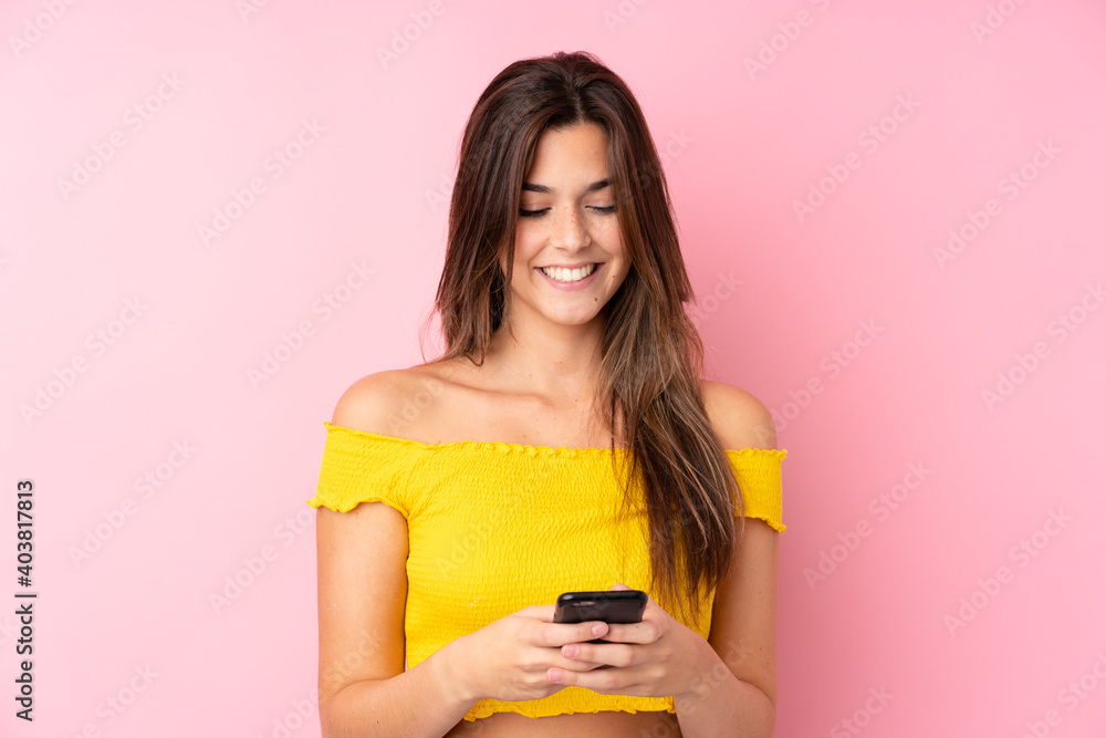 Teenager Brazilian girl over isolated pink background sending a message with the mobile Teenager Brazilian girl over isolated pink background sending a message with the mobile